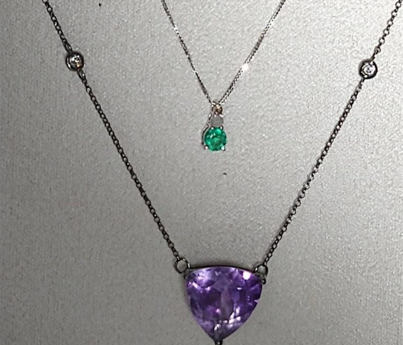 Amethyst and emerald pendants displayed together on darkened chains